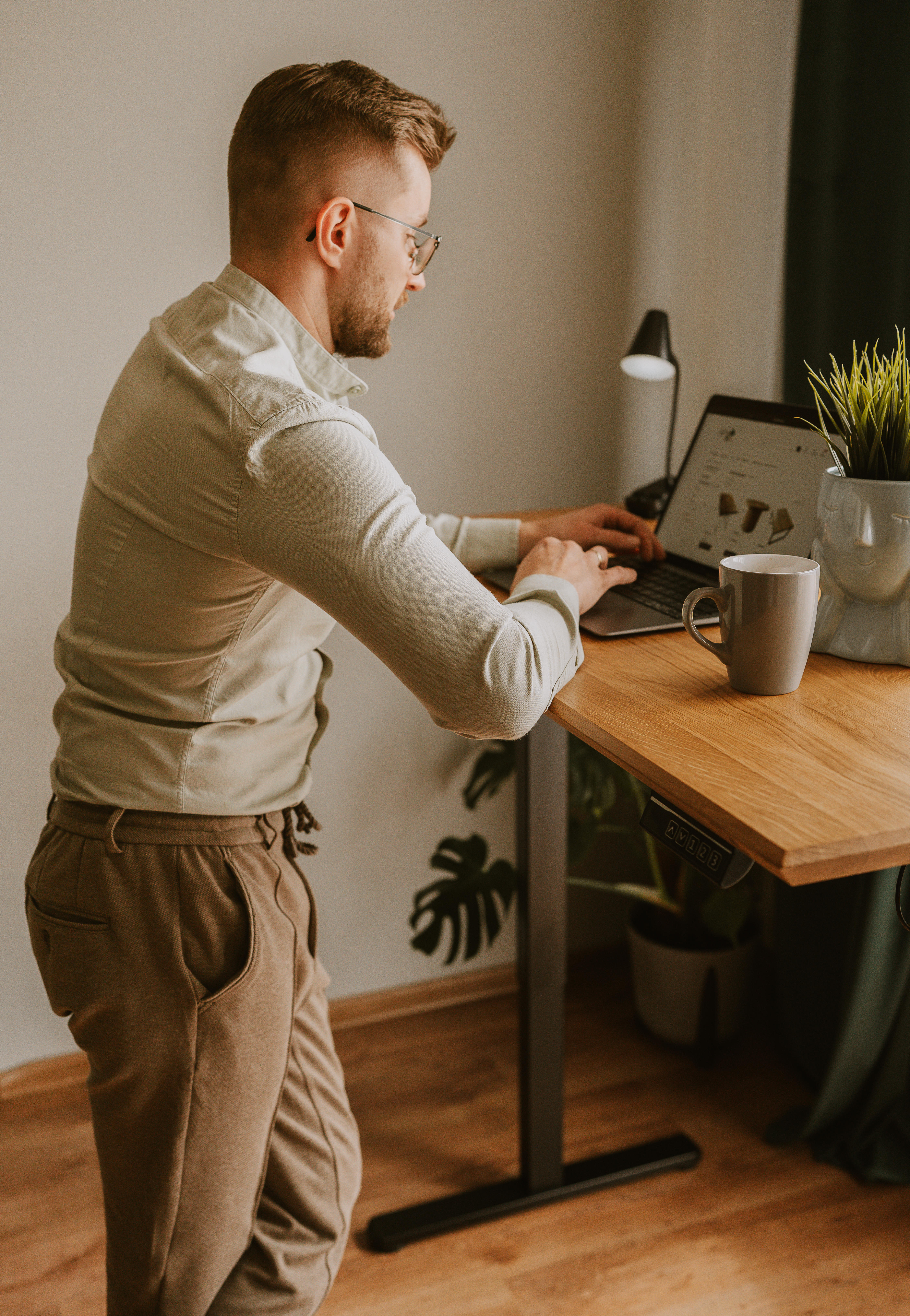alt="Osoba stojąca przy biurku IBIS z elektryczną regulacją wysokości, pracująca na laptopie – ergonomiczne stanowisko pracy"